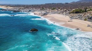 Una playa costera con aguas turquesas cristalinas, una orilla arenosa y afloramientos rocosos.