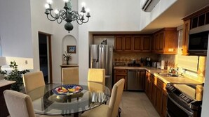 Una cocina moderna con una mesa de vidrio redonda para comer, armarios de madera y electrodomésticos de acero inoxidable.