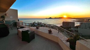 Una terraza con asientos al aire libre, con vista a la puesta de sol sobre el océano.