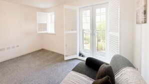 A room with a grey carpet, a sofa with a throw blanket, and a ceiling light fixture. - Your Bromley Experience  (Bromley)