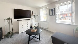 A modern living room with a flat-screen TV, a round black table, a grey sofa, and a view of the city through large windows. - Your Bromley Experience  (Bromley)