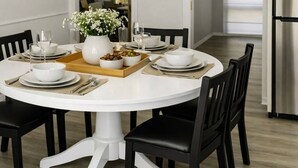 Un tavolo da pranzo rotondo con piatti bianchi, sedie nere e un vaso bianco al centro con fiori.