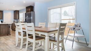 A modern kitchen with a dining area, featuring a wooden table, white chairs, and a built-in refrigerator. - New Remodel on Black River with Hot Tub, Kayaks, Gym, Fireplace, & Game Room (South Haven)