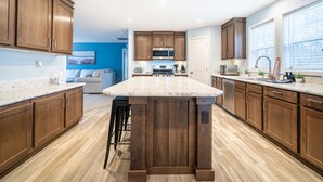 A kitchen with wooden cabinets, a marble countertop, and a central island. - New Remodel on Black River with Hot Tub, Kayaks, Gym, Fireplace, & Game Room (South Haven)