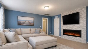 A living room with a sectional sofa, a flat-screen TV, a fireplace, and a framed picture on the wall. - New Remodel on Black River with Hot Tub, Kayaks, Gym, Fireplace, & Game Room (South Haven)
