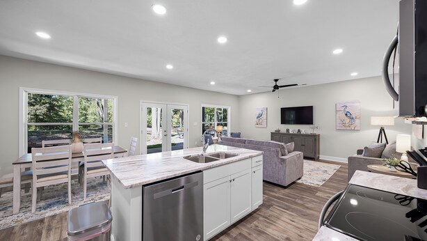 A modern kitchen with a dishwasher, a dining area with a bench, a gray sofa, and a TV in the living room. - 4-bedroom Chalet Overlooking Pickwick Landing Golf Course (Counce)