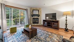 Una sala de estar con chimenea, televisor y un ventanal grande con vistas a un jardín.