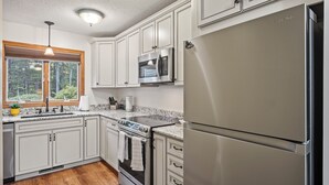 Una cocina moderna con electrodomésticos de acero inoxidable, armarios blancos y un amplio ventanal con vistas al exterior.