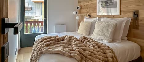 A bedroom with a wooden headboard, a large bed with white bedding, a beige throw blanket, and a framed picture on the wall.