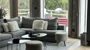 Ein modernes Wohnzimmer mit einem grauen Sofa, zwei Beistelltischen und einem Couchtisch. Große Fenster bieten einen Ausblick ins Freie.