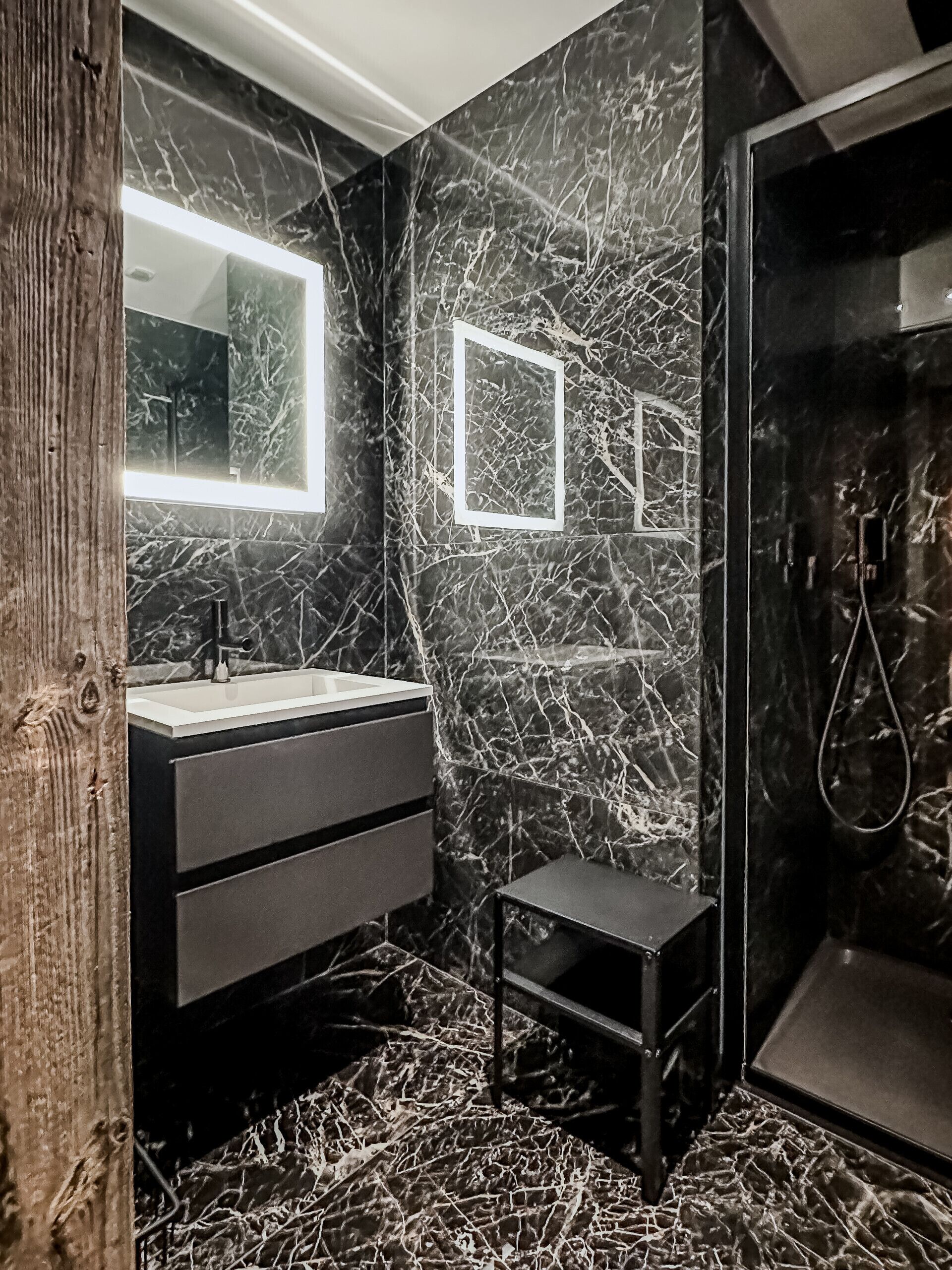 Un baño moderno con salpicadero de mármol, un espejo grande, tocador con lavabo y zona de ducha.