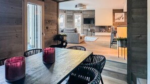 Ein moderner Essbereich mit einem Holztisch, schwarzen Stühlen, einem Kamin und einer Küche im Hintergrund.