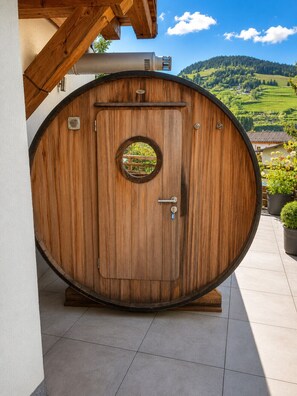 Une porte en bois, en forme de tonneau, ornée d’une fenêtre circulaire, d’une poignée et d’un trou de serrure, le tout se détachant sur un paysage pittoresque en arrière-plan.