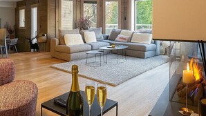 Ein modernes Wohnzimmer mit einer Couch, einem Couchtisch und einem Kamin. Auf dem Tisch stehen Kerzen und eine Schale mit Obst.