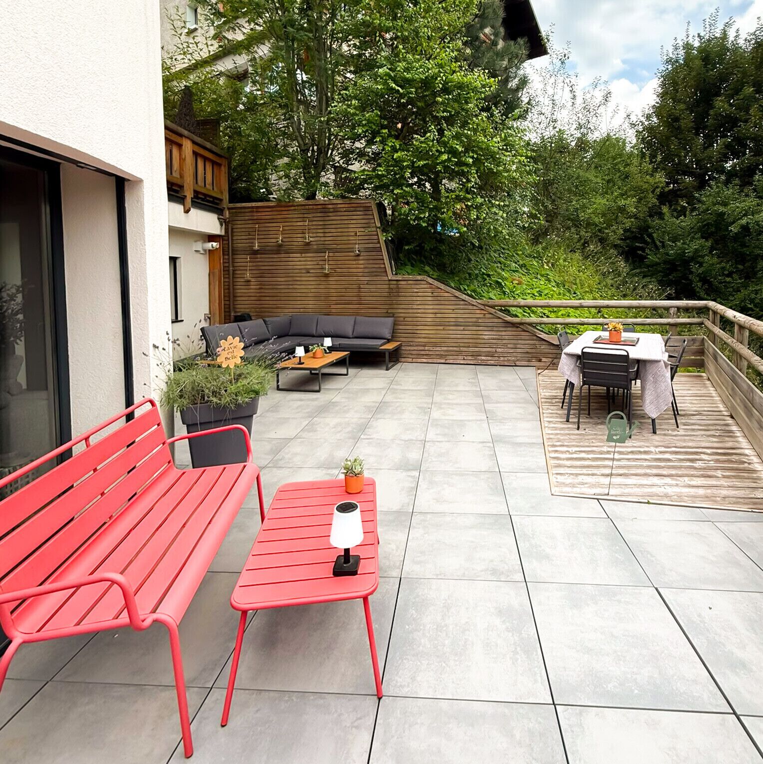 Un patio al aire libre con un banco rojo, una mesa pequeña con una lámpara, un sofá y una zona de comedor con sillas y una mesa.