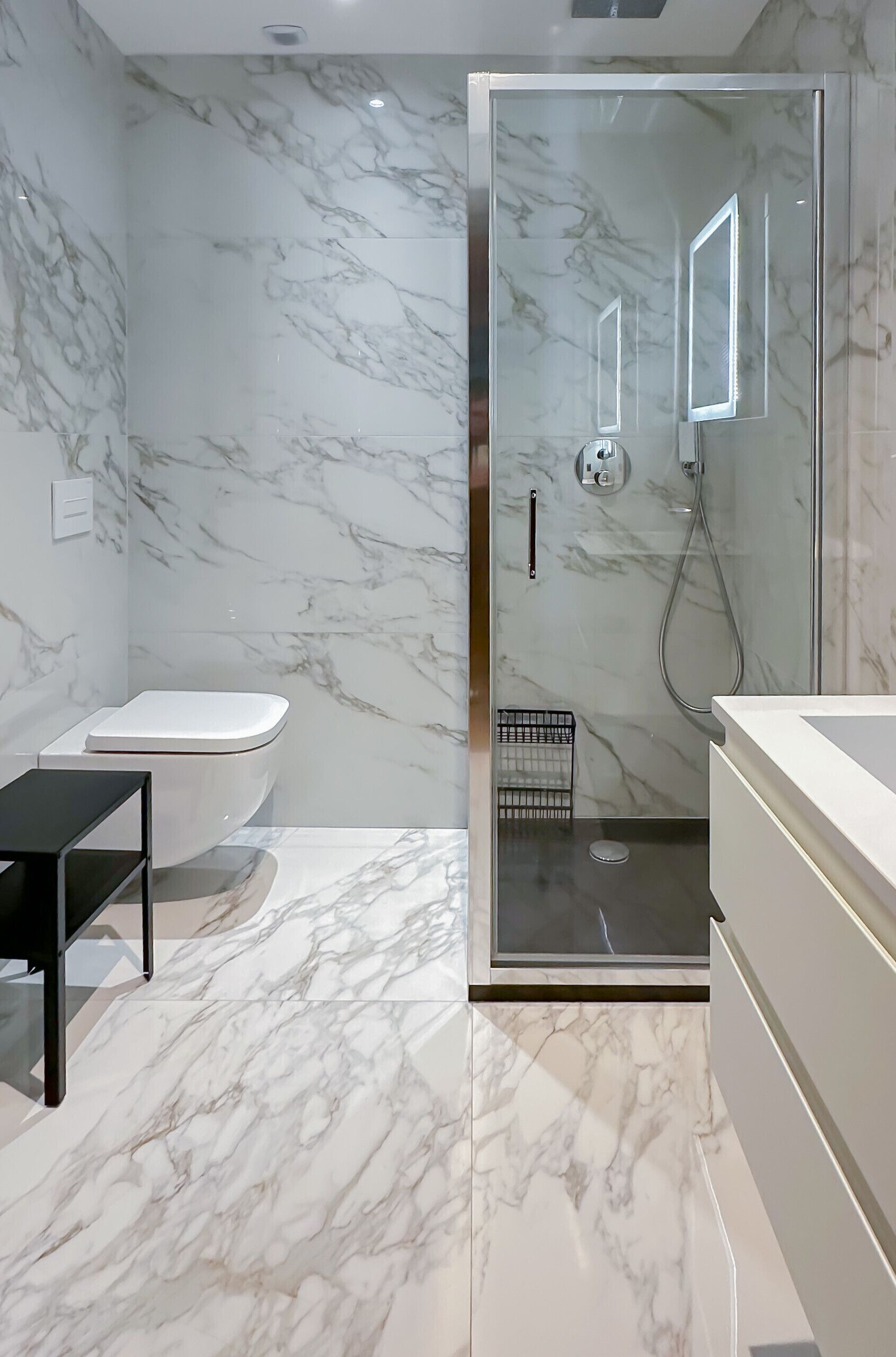 A modern bathroom with a marble floor, a glass-enclosed shower, a toilet, and a vanity with a mirror.