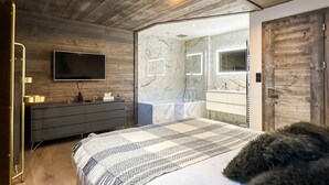 Ein modernes Schlafzimmer mit Holzbalkendecke, einem großen Bett, einem Fernseher, einem Badezimmer mit Marmorwänden und einer Holztür.