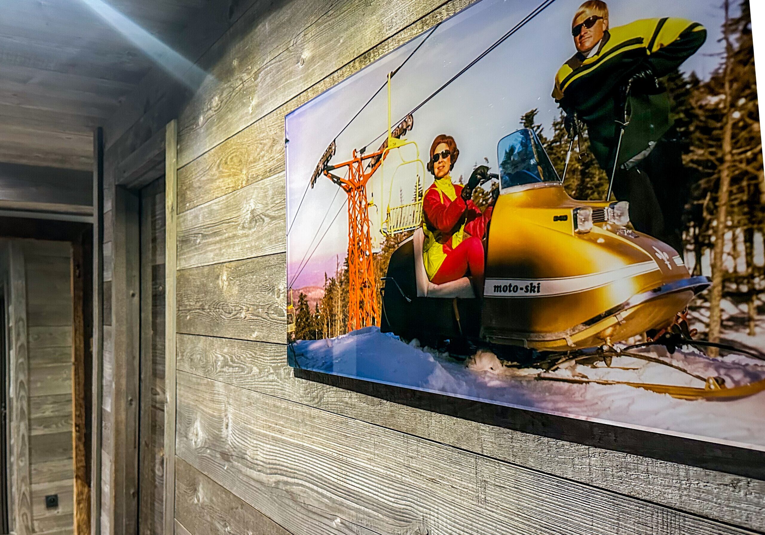 Un muro con un poster che ritrae una persona su una moto, un veicolo giallo e un paesaggio innevato.