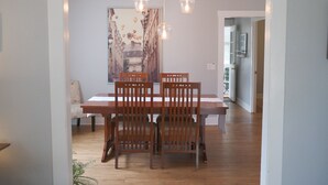 Een eetruimte met een houten tafel en stoelen, hanglampen en een groot schilderij aan de muur.
