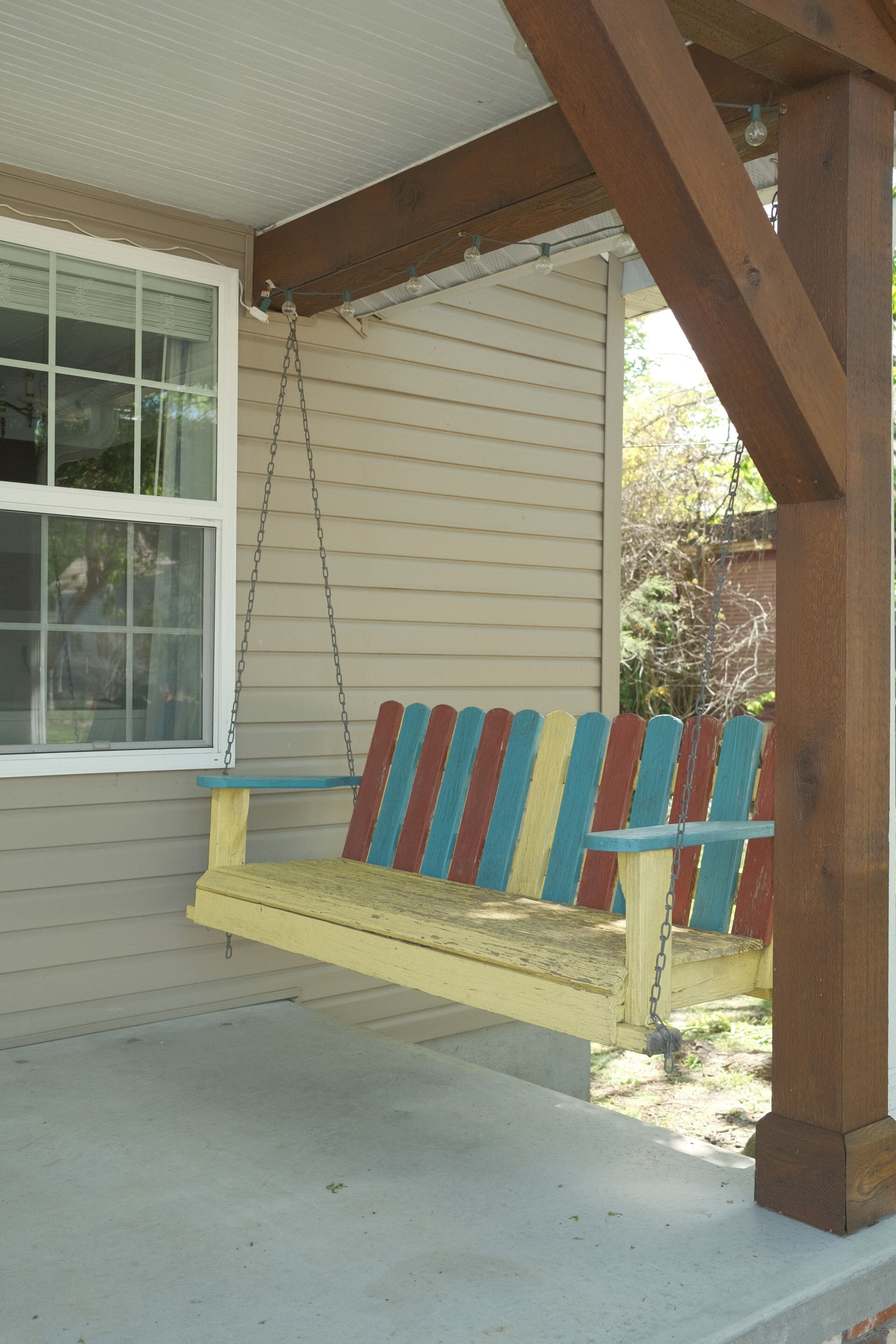 A porch with a swing, a window, and a wooden structure.