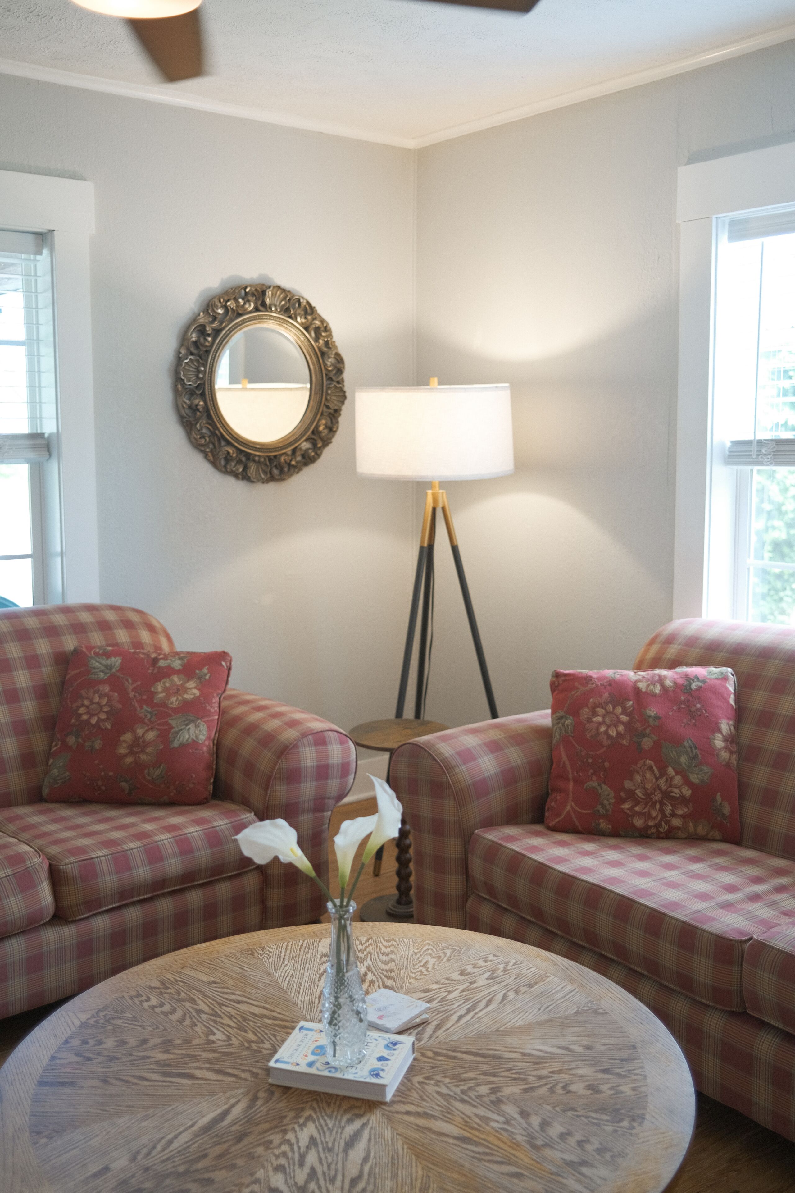A living room with a round coffee table, two plaid sofas, a mirror, and a floor lamp.