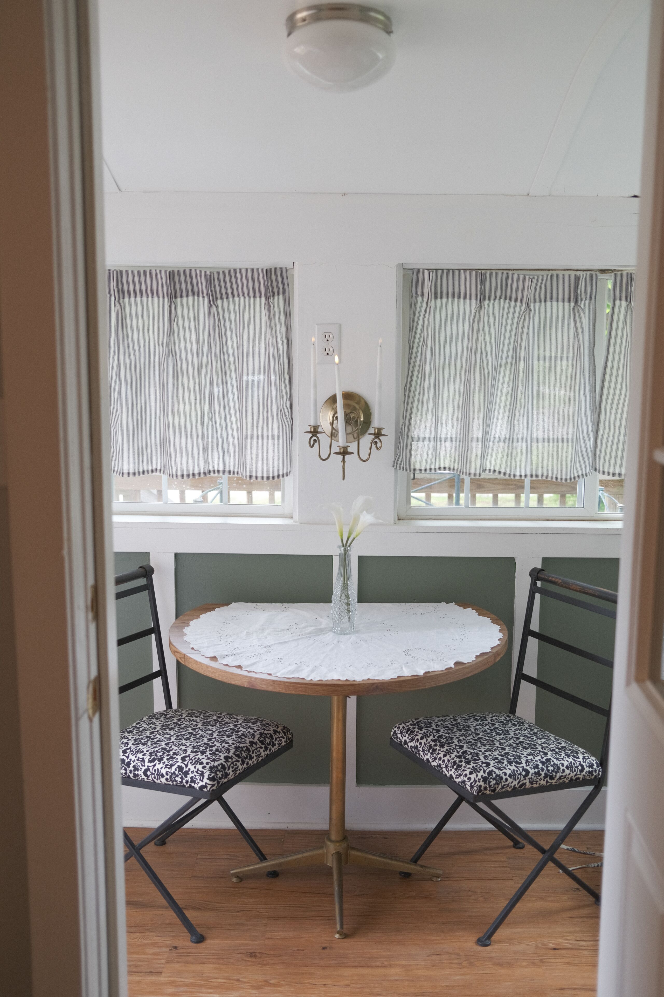 Een kamer met een ronde tafel, twee stoelen, een vaas met bloemen en een raam met gordijnen.