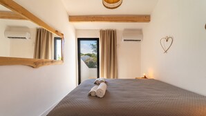 A bedroom with a large bed, a mirror, an air conditioning unit, a heart-shaped decoration, and a view through a door.