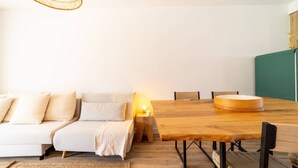 A cozy living area with a wooden dining table, a sofa, and a woven light fixture.