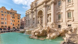Une fontaine historique à l’architecture classique, entourée d’immeubles et de touristes.
