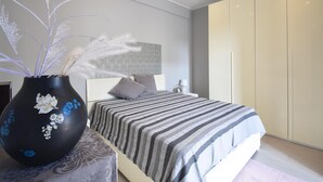 Une chambre à coucher moderne avec un lit, une table de chevet, une grande armoire et un vase décoratif contenant des plantes séchées.
