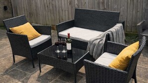 A wicker outdoor seating area with cushions, a glass table, and a bottle of wine. - Large 6-Bed House | 2 Bathrooms | Parking | Garden (Bristol)
