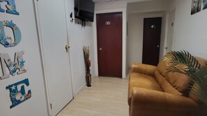 Een gang met een bruine leren bank, een houten deur met de aanduiding 'C2', en een muur met decoratieve letters en een klein plantje.