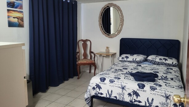 Een slaapkamer met een bed, een stoel, een klein tafeltje en een spiegel.