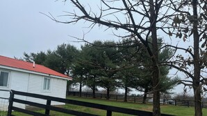 A white building with a red roof, surrounded by a fenced area with trees and grass. - Charming 3-bedroom detached cottage on horse farm near Lexington and Georgetown. (Paris)