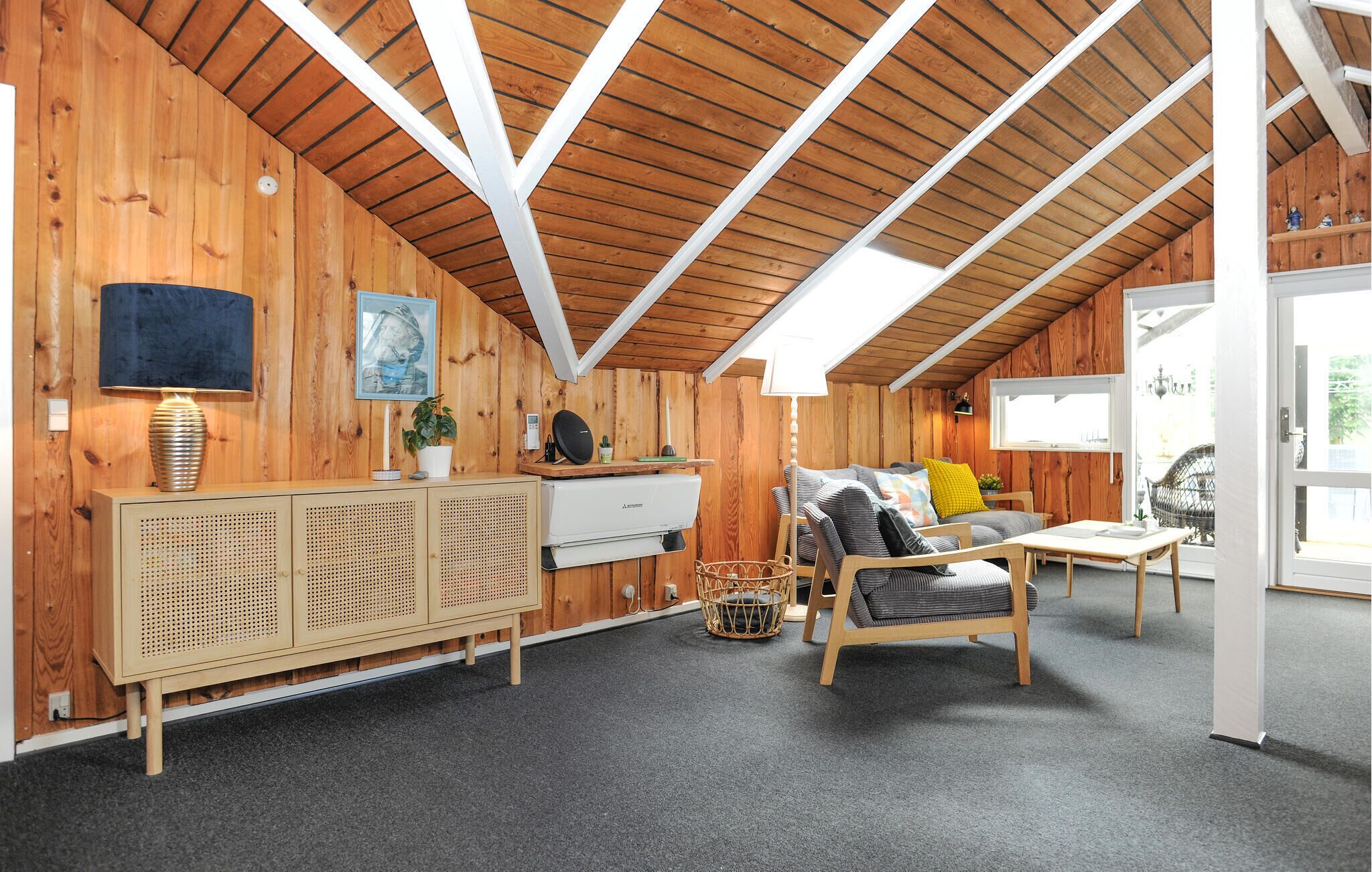 Une pièce chaleureuse avec des murs en bois, un plafond en pente, un canapé, une petite table, un meuble et une fenêtre.