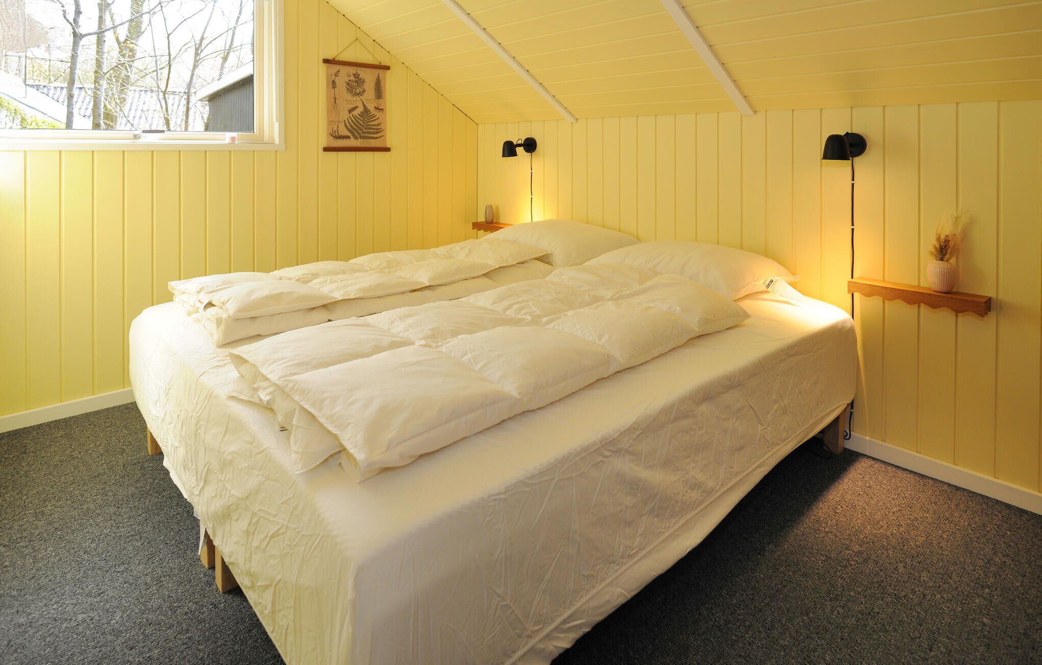 A single bed in a room with yellow walls, a window, and a wall-mounted lamp.