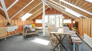 A cozy, wooden interior with a high ceiling, a dining area with a long table and chairs, a sofa with cushions, and a small kitchen area with a stove and cabinets. - 3 bedroom amazing home in Toftlund (Toftlund)