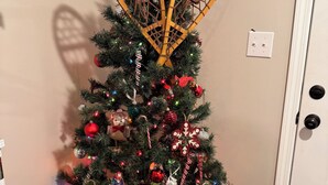 A Christmas tree with ornaments and a star on top, placed in a corner of a room with a wooden floor and a white door. - Peaceful Woodland charm 12 minutes from Corbin/London, 18 minutes from I-75 (Lily)