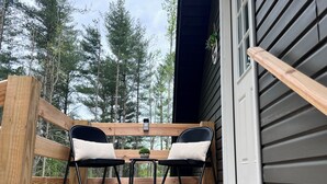 A wooden deck with two black chairs and a small table, overlooking a forested area. - Peaceful Woodland charm 12 minutes from Corbin/London, 18 minutes from I-75 (Lily)