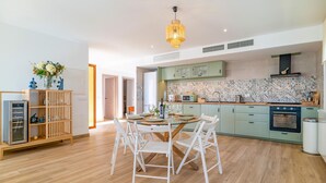 A modern kitchen with a dining area, featuring light green cabinets, a patterned backsplash, and a wooden dining table with white chairs. - Gorgeous home in Mijas (Mijas)