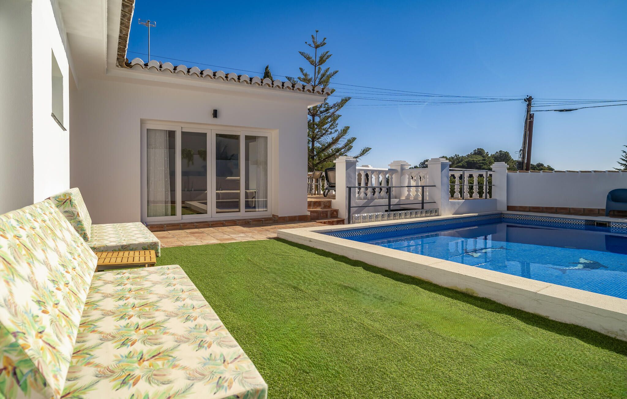 A poolside area with a white building, a green lawn, and a clear blue sky.