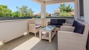 Een overdekt terras met rieten meubels en een tafel met glazen blad.