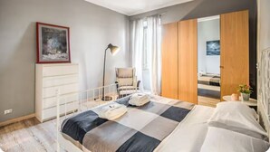 Une chambre à coucher moderne avec un grand lit, une lampe de chevet, une chaise, une armoire et un tableau au mur.