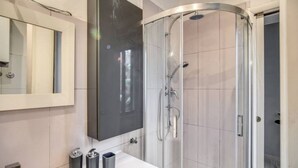 Une salle de bain moderne avec une douche à parois de verre, un grand miroir et un plan de toilette blanc doté de deux distributeurs de savon.