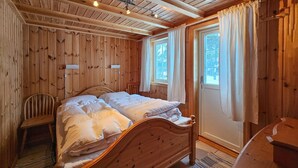 A wooden-paneled bedroom with a bed, a chair, and a window with curtains.