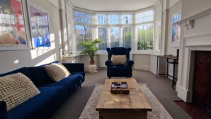 Een woonkamer met een blauwe bank, een houten salontafel, een blauwe fauteuil en een open haard.