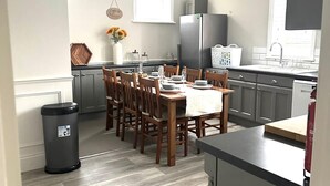 Een moderne keuken met een eethoek, met een centraal kookeiland, houten stoelen en een roestvrijstalen koelkast.