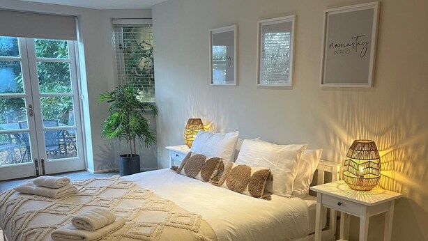 Een slaapkamer met een groot bed, twee nachtkastjes, een kamerplant en kunstwerken in een lijst aan de muur.