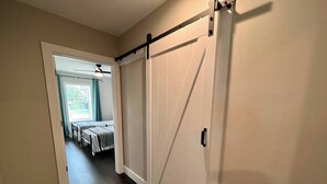 A hallway with a sliding barn door leading to a room with two beds and a table.