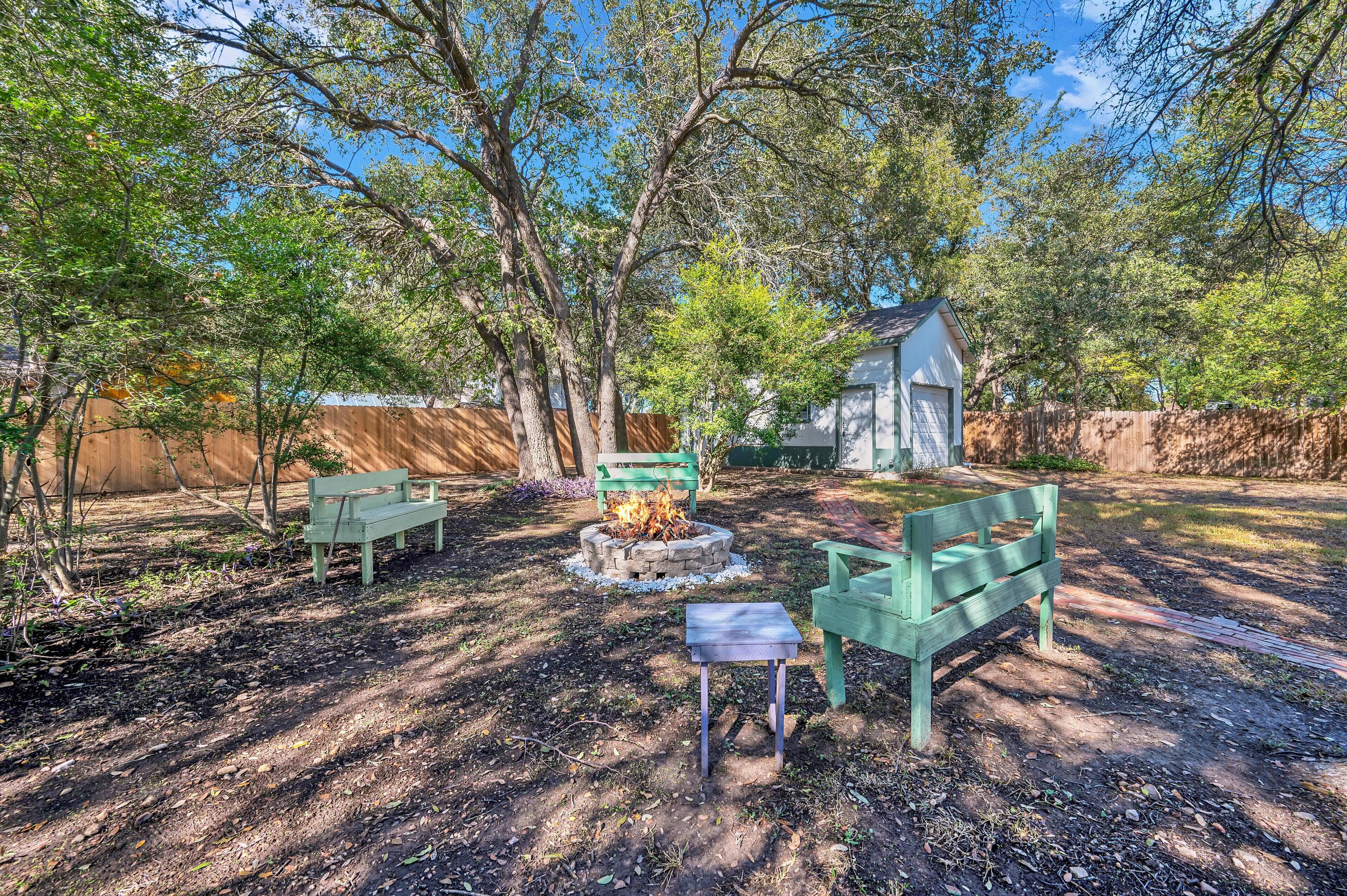 A backyard with a fire pit, two green benches, and a small shed.